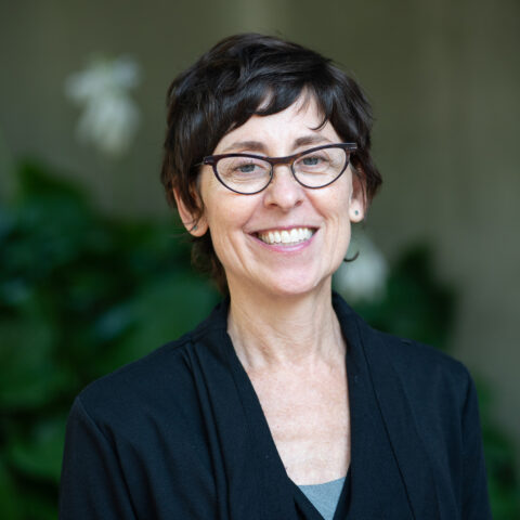 Smiling woman wearing a black blazer in front of green trees